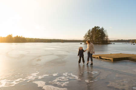 Mother and her little daughter scating on th eice of a frozen lake in the light of a sunny afternoon in winter.の写真素材