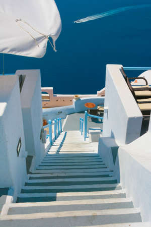White street with long staircase and traditional architecture on island of Santorini in Fira, Greece. Aegean sea in the background.の写真素材