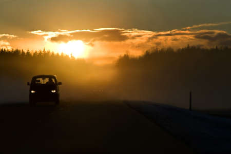 Fog on the road at the start of winter. Bright sun in clouds, minivan on the left side of road and dangerous overtaking in the background. This is E22/A10 winter road Riga - Ventspils. の写真素材