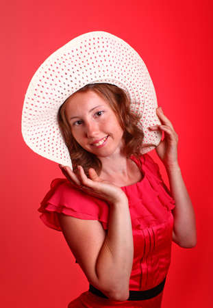 Adorable woman in beautiful red dress and summer hat. Portrait on a red background.の写真素材
