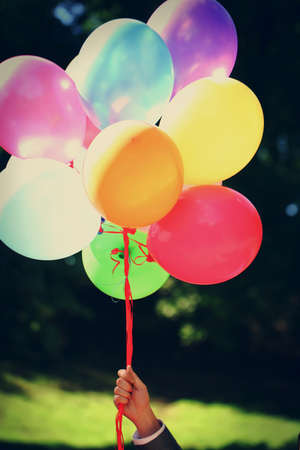 Multi colored party balloons are ready to fly away to the sky, but groom is holding them in hand.