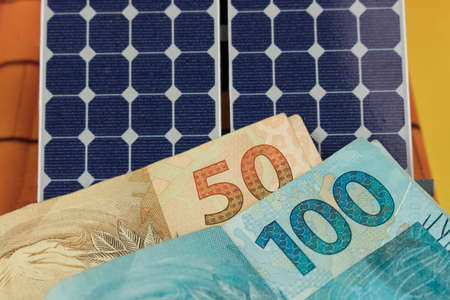 Solar panel with 50 and 100 bills of Brazilian money and coins.の写真素材