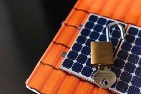 Padlock with key on photovoltaic solar panel on black background.