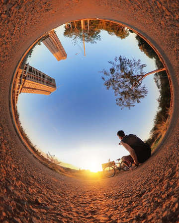 Mini planet of a park and sunset.Man with bicycle on little planet with trees, soft blue sky and sunset.の写真素材