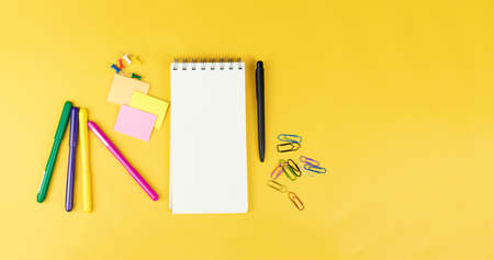 Top view of blank notebook and school supplies like colored markers, sticker and clipers on yellow background, space for textの写真素材