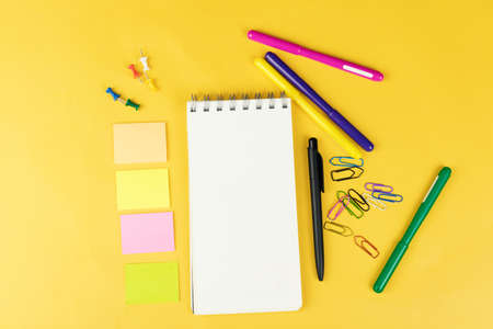 Top view of blank notebook and school supplies like colored markers, sticker and clipers on yellow...