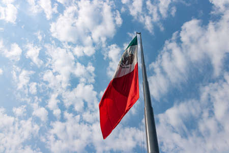 Mexican flag fluttering over a cloud sky on a sunny day.