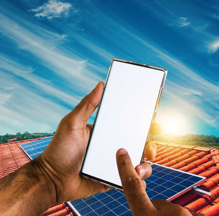 Male hands holding a mobile with solar energy photovoltaic panel at backgroundの写真素材