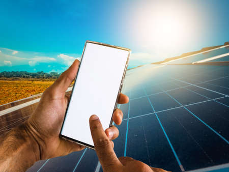 Male hands holding a mobile with solar energy photovoltaic panel at backgroundの写真素材