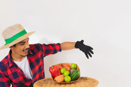 Farmer black man with hat and gloves holding a basket of vegetables (carrot, lemon, tomatoes, chayote and beet) isolated in white backgroundの写真素材