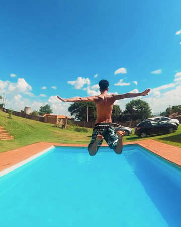 Black man jumping in the pool on sunny dayの写真素材
