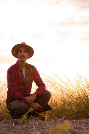 Farmer with hat in farm plantation on sunset. Buildings and city blurred background.