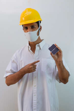Worker with helmet and pandemic mask isolated on white background. Black man holding photovoltaic panel.の写真素材