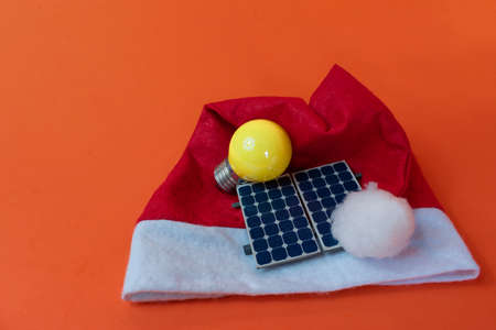 Chistmas Santa Claus hat with photovoltaic solar panel and lamp isolated on orange background.の写真素材
