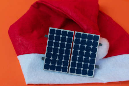 Chistmas Santa Claus hat with photovoltaic solar panel and lamp isolated on orange background.