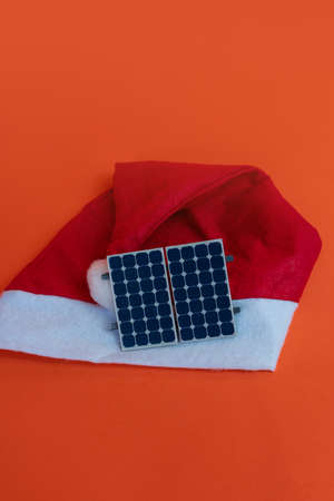 Chistmas Santa Claus hat with photovoltaic solar panel and lamp isolated on orange background.