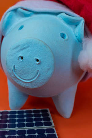 Piggy bank coins with Santa Claus christmas hat, photovoltaic solar panel and lamp isolated on...
