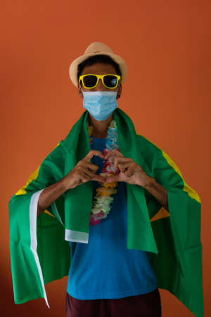 Black man in costume for carnival with brazil flag and pandemic mask isolated on orange background.の写真素材