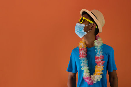 Black man in costume for carnival with pandemic mask isolated on orange background.