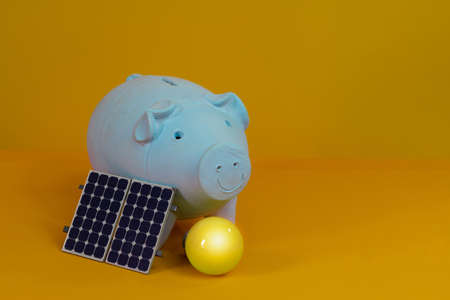 Piggy bank, yellow lamp and photovoltaic solar energy panel isolated on yellow background.