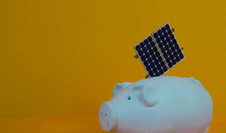 Piggy bank and photovoltaic solar energy panel isolated on yellow background.の写真素材