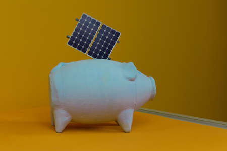Piggy bank and photovoltaic solar energy panel isolated on yellow background.