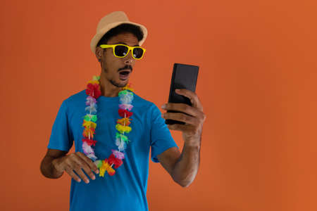 Black man in costume for brazil carnival holding mobile isolated on orange background.の写真素材