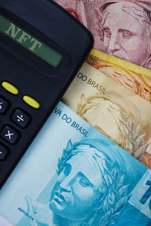 NFT written in calculator with brazilian money background.