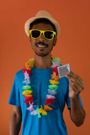 Black man in carnival costume holding  a condom isolated on orange background.の写真素材