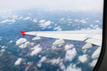 Wing of an airplane flying above the city. The view from an airplane window. Cloudy and color sky...