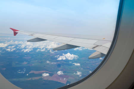 Wing of an airplane flying above the city. The view from an airplane window. Cloudy and color sky...