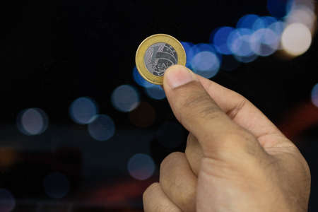 Holding a Brazilian money coin at a blurry lights backgroundの写真素材