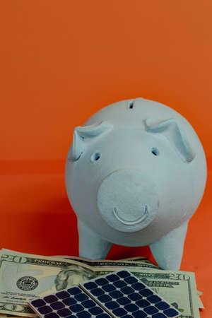Piggy bank with dollar bill and photovoltaic solar panel isolated on orange background. Solar Energy Concept Image.の写真素材