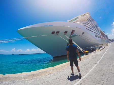 Portrait of a young black male tourist in front of a cruise ship on cloudy sky.の写真素材