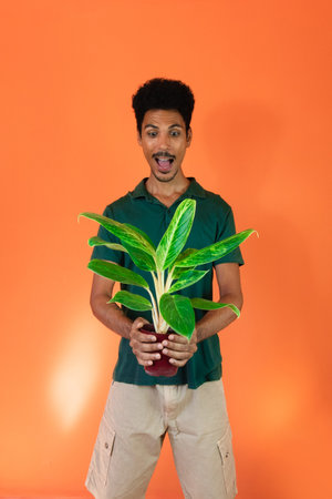 Handsome Black man with green shirt holding plant isolated on orange background.