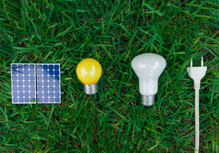 Photovoltaic solar panel, lamp, plug wire and mobile on green grass background. Alternative clean and renewable energy concept.の写真素材