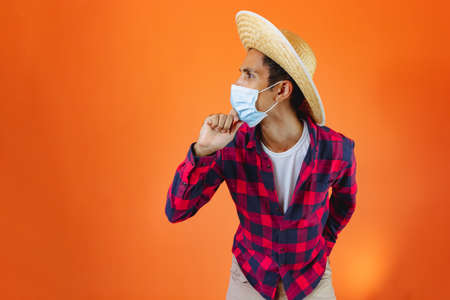 Black Man With Junina Party Outfit and pandemic mask Isolated on Orange Background. Young man...