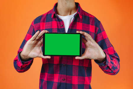 Black Man With Junina Party Outfit holding a tablet Isolated on Orange Background. Young man wearing...