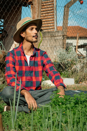 Black farmer beside small modest vegetable garden on sunny day. Farmer With Hat on farm.の写真素材