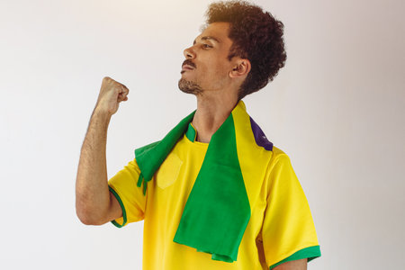 Brazilian Black Man Fan with Soccer Team Shirt Isolated on White. Sport Fan With Flag Celebrating...
