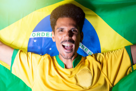 Brazilian Football Fan - Black Man Holding Brazil Flag Behind Celebratingの写真素材