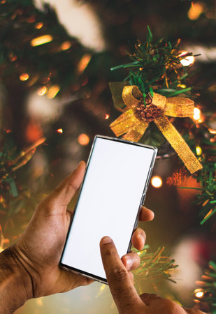 Holding a Mobile On a Christmas Background. Black Hands With Blanck Cell Phone Screen, Space for Text.の写真素材
