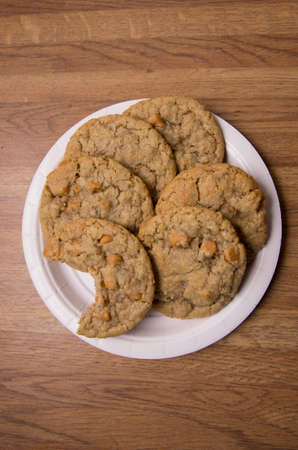 Oatmeal cookies with Butterscotch chips arranged on a paper plate, one cookie bitten into.
