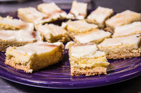 Cream cheese lemon bars on a purple plate, sliced and ready to serve.