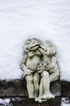 A statue of kissing frogs sits on a wall, covered with snow.の写真素材