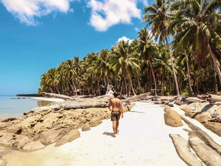 Man walking on the white beach and turquoise water with clear blue sky and lots of palm trees on Sicsican Island in Balabac, Palawan, Philippinesの写真素材