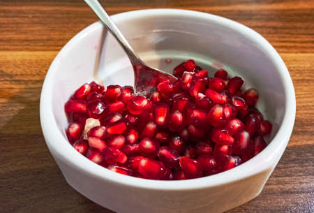Group of fresh red pomegranate seeds isolated on the white cup with wooden background.の写真素材