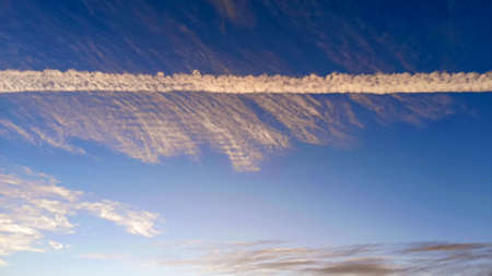 Pattern of airplane trails cutting blue sky in half. Airplane leaving behind a long white trail at...