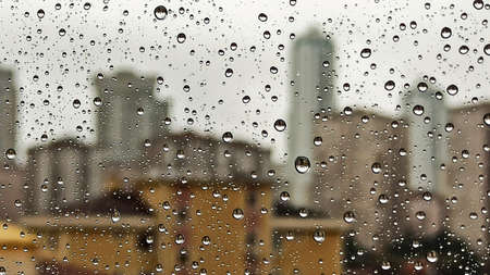 Raindrops on office window with blur gray sky background. Office window covered with closeup rain...