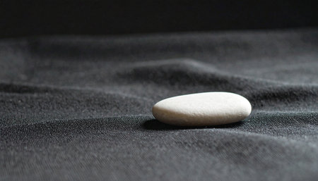 Realistic single smooth white pebble placed on dark black textured fabric with natural diffused light, minimal calm compositionの素材